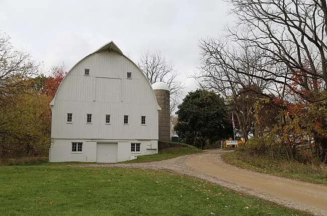 A white gambrel-roof barn beside a gravel road